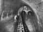 Brighton & Hove intercepting sewer in 1939. It shows the meeting point of the London Road and Lewes Road Valley sewers. Two workmen can be seen standing in the tunnel entrances at the rear of the sewer. Water is running down through these tunnels while another workman attends to the overflow area on the left of the photograph. The tunnels visible at the rear of the photograph are approximately 2.5 metres high. If the water was too high, it would fill into the 27 metre overflow channel (Brighton & Hove Museum)
