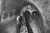 Brighton & Hove intercepting sewer in 1939. It shows the meeting point of the London Road and Lewes Road Valley sewers. Two workmen can be seen standing in the tunnel entrances at the rear of the sewer. Water is running down through these tunnels while another workman attends to the overflow area on the left of the photograph. The tunnels visible at the rear of the photograph are approximately 2.5 metres high. If the water was too high, it would fill into the 27 metre overflow channel (Brighton & Hove Museum)